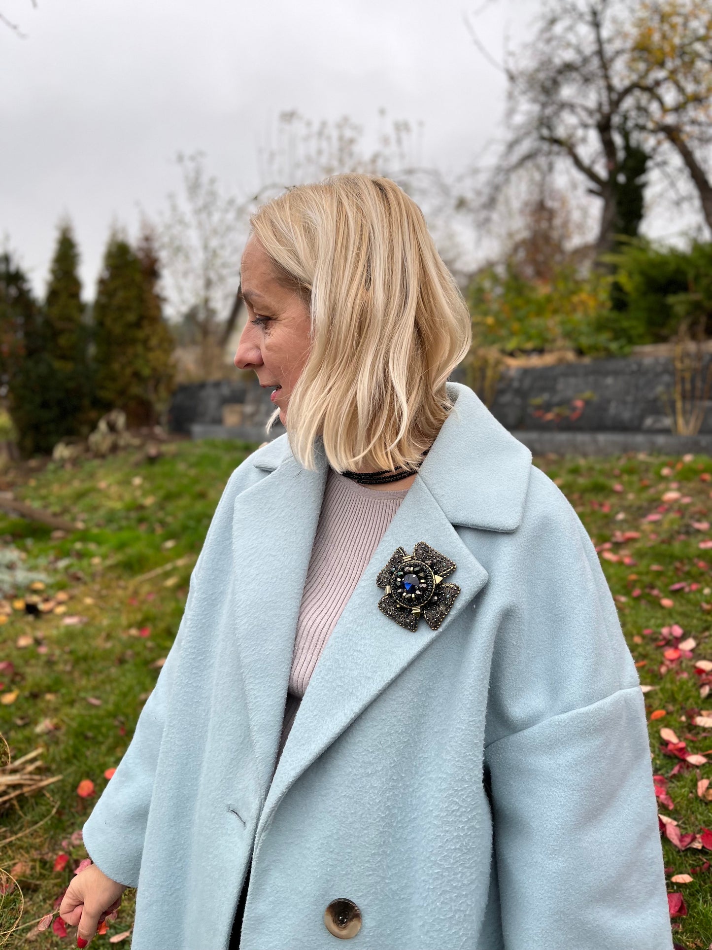 Moteris dėvi, rankų darbo vienetinę mėlynos ir žalvario spalvos sagę.